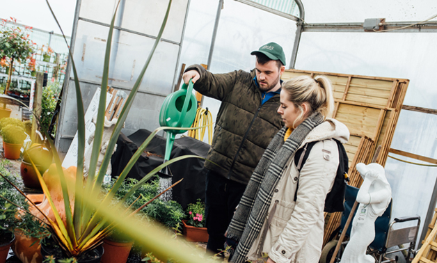 a man stands beside a woman in a greenhouse while watering a plant